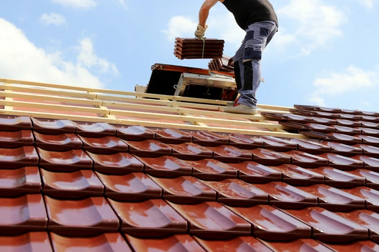 Ouvrier couvreur installant des tuiles terre cuite sur charpente bois, travaux de toiture en cours