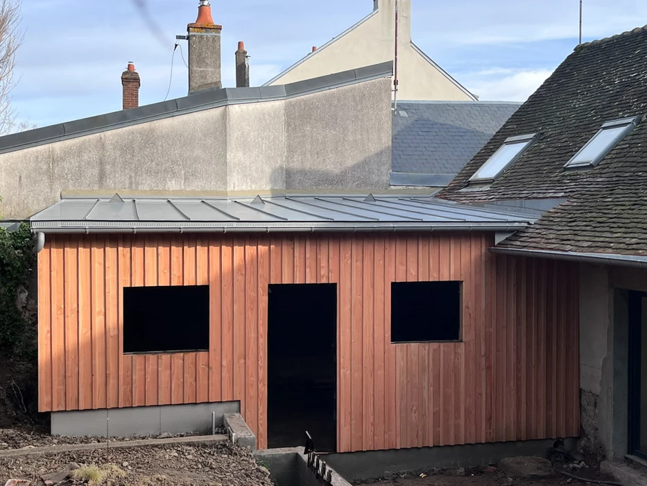 Extension bois contemporaine en cours de construction, bardage vertical en red cedar, toiture plate avec couverture en zinc à joint debout, chéneau aluminium