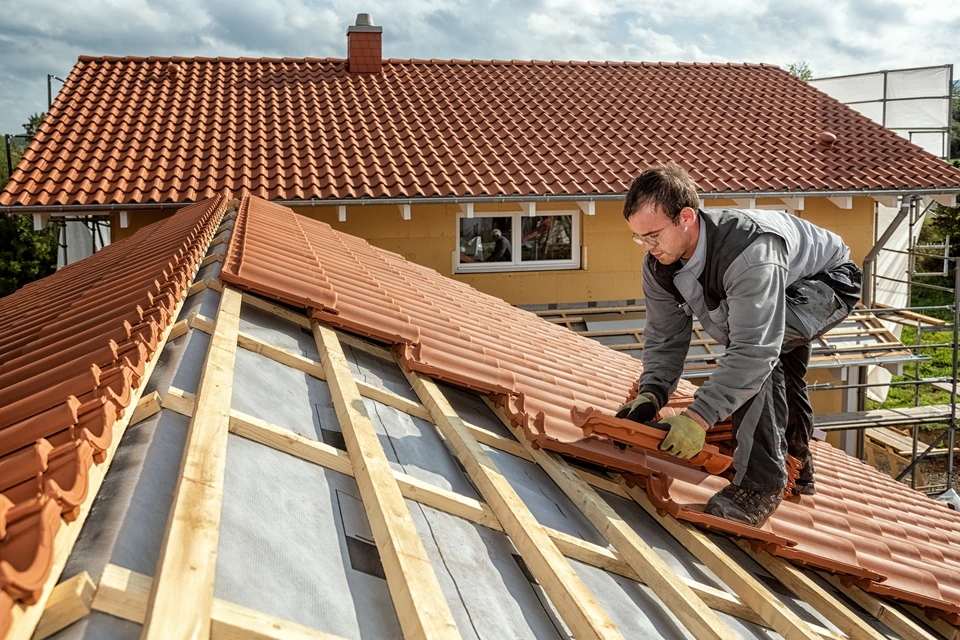 Ouvrier couvreur installant des tuiles terre cuite sur toiture en construction, travaillant sur charpente bois avec membrane d'&eacute;tanch&eacute;it&eacute;