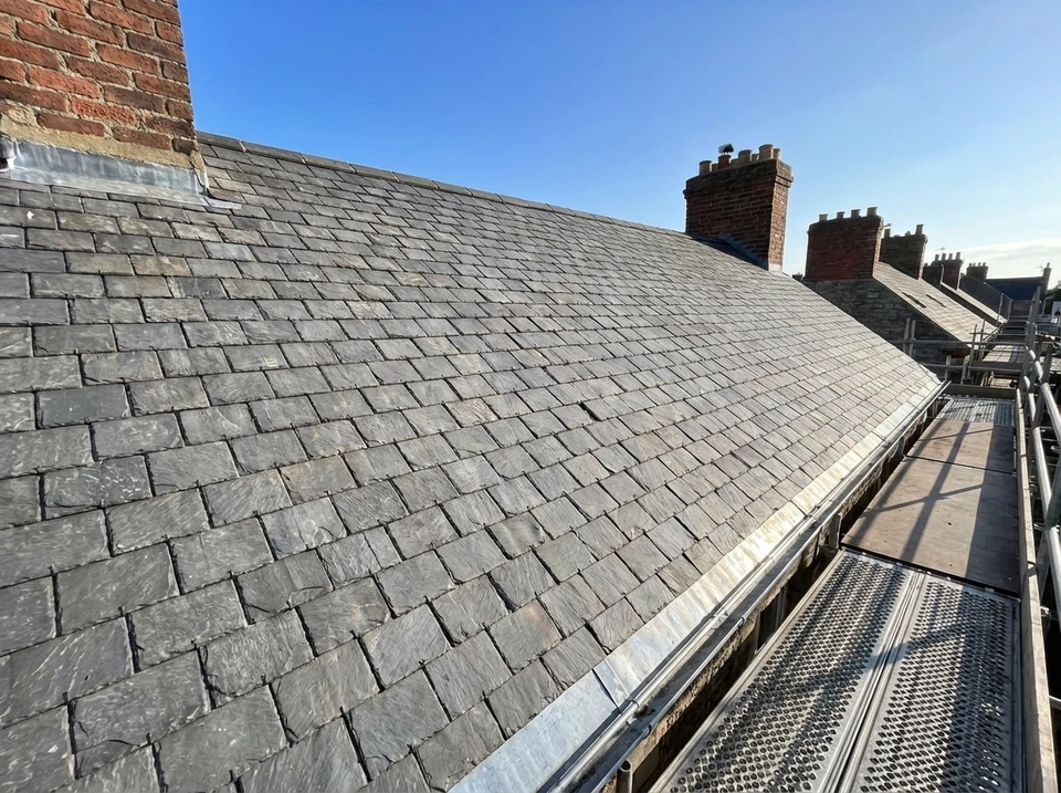 Chantier de couverture en cours avec ouvriers installant des tuiles terre cuite rouge sur charpente bois