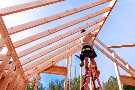 Chantier de construction ext&eacute;rieur montrant une charpente en bois en cours d'assemblage sous ciel bleu