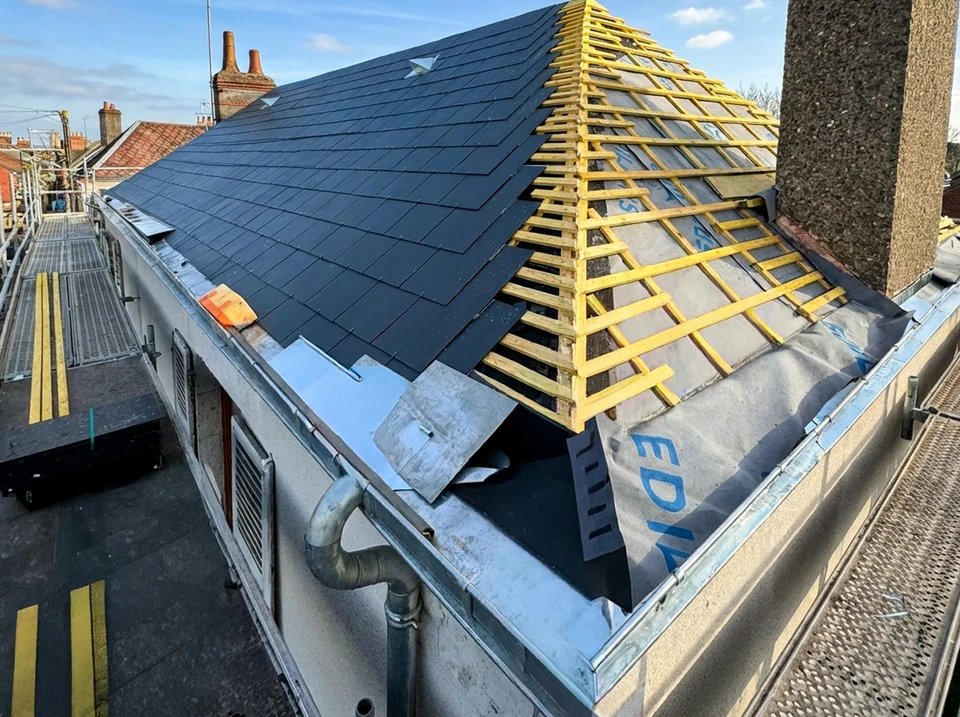 Homme en équipement de sécurité nettoyant une toiture de tuiles rouges avec un nettoyeur haute pression