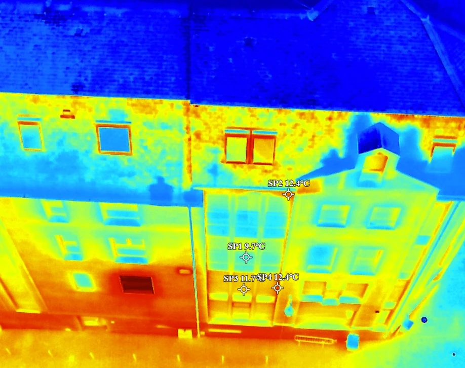 Mains tenant une tablette numérique affichant une thermographie infrarouge d'une maison moderne avec toiture en bois et façade blanche